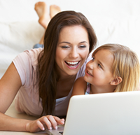 A smiling mother and her child on the bed looking at computer screen