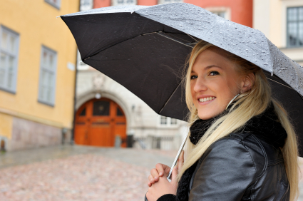 young woman smiling with whitened teeth holding an umbrella in the rain