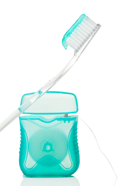 close up of a toothbrush with toothpaste on it leaning against dental floss container