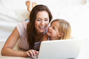 woman and child on bed looking at a computer screen to book dentist for children appointment