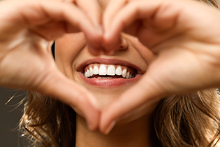 A woman who is forming a heart with her hands to frame her perfect smile